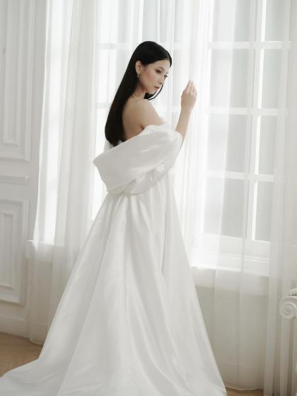 Bride in an off-shoulder lace wedding gown by a bright window by CELRA